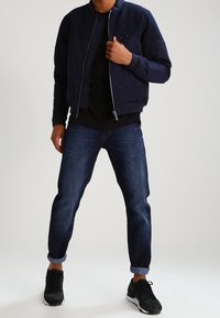 Chaqueta bomber de marina con cremallera frontal, combinada con jeans azul oscuro arremangados y zapatillas deportivas negras. Tejido suave, corte casual.
