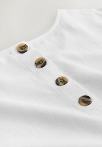 Hvid linned skjorte med en buet halsudskæring og tre brune mønstrede knapper langs klappen. Blød tekstur med en let, åndbar fornemmelse.