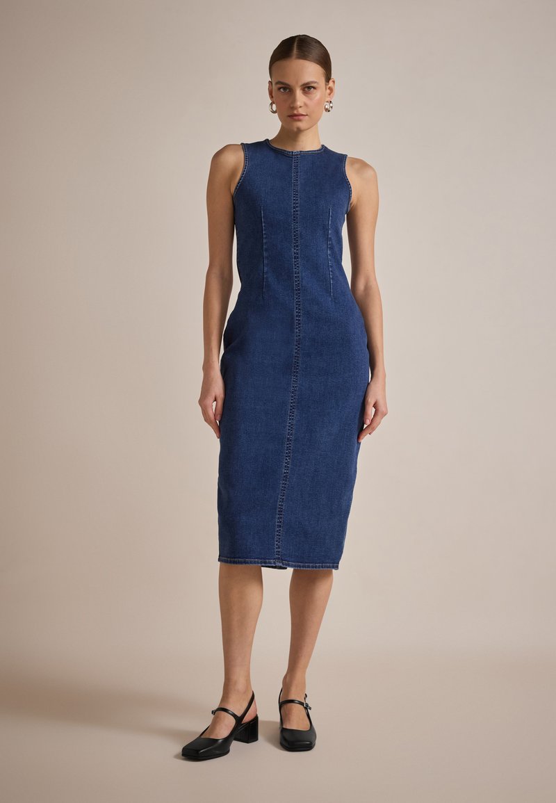 Denim midi-kjole, tettsittende design med ermeløs snitt, med en sentral søm og kontrasterende søm, i en dyp indigo farge.