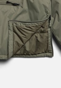 Olivgrön pufferjacka med insida och dragkedjeficka samt kviltad foder, som visar en mjuk och lätt syntetisk tyg.