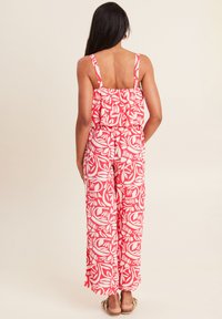 Combinaison à motifs rouge et blanc avec un haut volanté, des fines bretelles et un design à jambes larges. Le tissu semble léger avec une texture lisse.