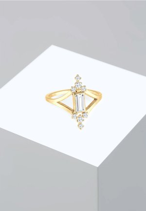 Gouden ring met een centraal smaragdgeslepen steen omringd door kleinere heldere stenen, met een open geometrisch bandontwerp.
