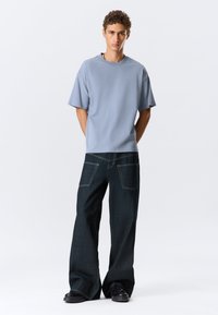 Světlomodré bavlněné tričko s krátkým rukávem, spárované s tmavými denimovými kalhotami širokého střihu a viditelnými zadními kapsami. Černé boty.