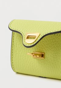 Πορτοφόλι από δέρμα με υφή σε χρώμα ασβέστη πράσινο, με κυματιστό καπάκι, χρυσή στερέωση και μαύρη λεπτομέρεια στις άκρες. Λεπτομέρειες με λείο φινίρισμα.