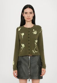 Vihreä neulecardigan, jossa on pitkät hihat, pyöreä kaula-aukko ja mustat napit. Edessä keltainen kukka-embroidointi.