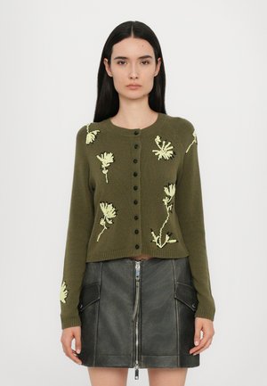 Grønn strikket cardigan med lange ermer, rund hals og svarte knapper, med gule blomsterbroderier på forsiden.