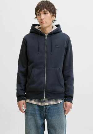 Marine blauwe zip-up hoodie van een katoenmix, met een fleece-gevoerde capuchon, voorzakken en een zwart logo-opkleding. Draagt over een geruit shirt.