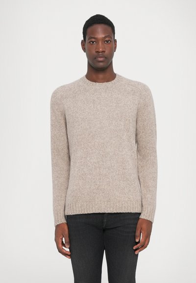 Pull beige en tricot avec un col rond et des manches longues. Tissu texturé avec des poignets et un ourlet côtelés. Porté avec un jean foncé.