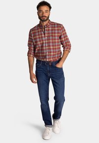 Rood en groen geruite overhemd, met knoopsluiting, gecombineerd met donkerblauwe jeans en witte sneakers, voorzien van een geweven riem.