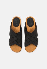 Svarta vävda halkskyddsandaler med en träsoffa och ilägg som visar ett strukturerat mönster. Har en korskorsdesign överst.
