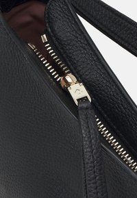Borsa in pelle nera con trama, con una cerniera dorata parzialmente aperta e un tirante della cerniera in pelle nera coordinato, su sfondo bianco.