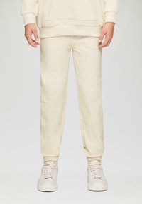 Cremefarbene Baumwoll-Sweatpants mit elastischen Bündchen und einem lockeren Schnitt, kombiniert mit passenden hellen Sneakern mit einer strukturierten Sohle.