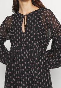 Musta pitkähihaine mekko, jossa on avainreikäkaulus, burgundin- ja valkoinen kukkakuosi sekä lentävä siluetti kevyestä kankaasta.