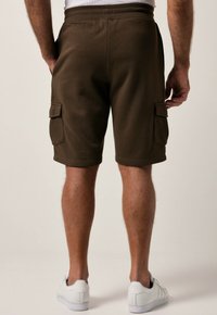 Braune Cargo-Shorts mit einem bequemen elastischen Bund und zwei Seitentaschen. Strukturiertes Material für einen lässigen Look, kombiniert mit weißen Turnschuhen.