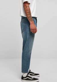 Blue denim jeans with a straight leg design, featuring a single back pocket and a slightly faded texture, paired with black sneakers.