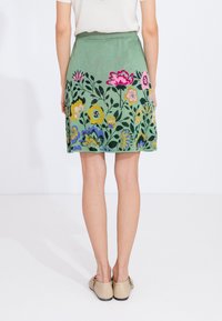 Jupe verte avec broderie florale en rose, jaune et bleu. Dotée d'une taille texturée et d'une coupe droite, avec une longueur au genou.