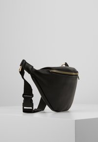 Sort læder trekantet taske med gylden lynlås, justerbar rem og flad bund. Glat tekstur med minimale hardware detaljer.