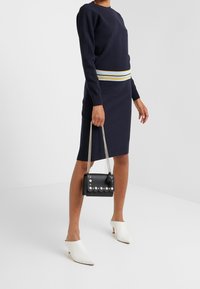 Vestito in maglia blu navy con una cintura a righe, abbinato a una borsa nera con dettagli in perle e un nappina, e mules bianche.