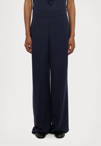 Marineblå vide bukser med en glat tekstur, høj talje og en afslappet pasform. Stoffet falder elegant ned til de sorte sko.