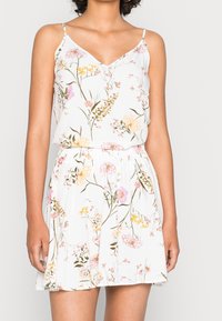 Abito floreale con sfondo bianco, caratterizzato da motivi rosa, gialli e verdi. Spalline sottili e vita elasticizzata. Tessuto leggero.