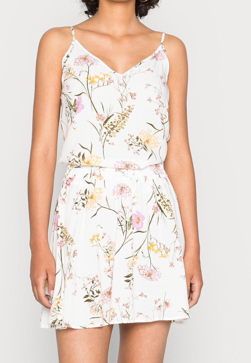 Abito floreale con sfondo bianco, caratterizzato da motivi rosa, gialli e verdi. Spalline sottili e vita elasticizzata. Tessuto leggero.