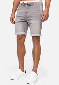 Shorts en denim gris avec ourlets retroussés, poches avant et arrière, taille ajustable avec un cordon noir et blanc. Associés à des baskets blanches.
