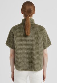 Kurzärmliger, olivgrüner Strickpullover. Texturiertes Material, hoher Kragen, lockerer Schnitt und gerade Saumlinie.