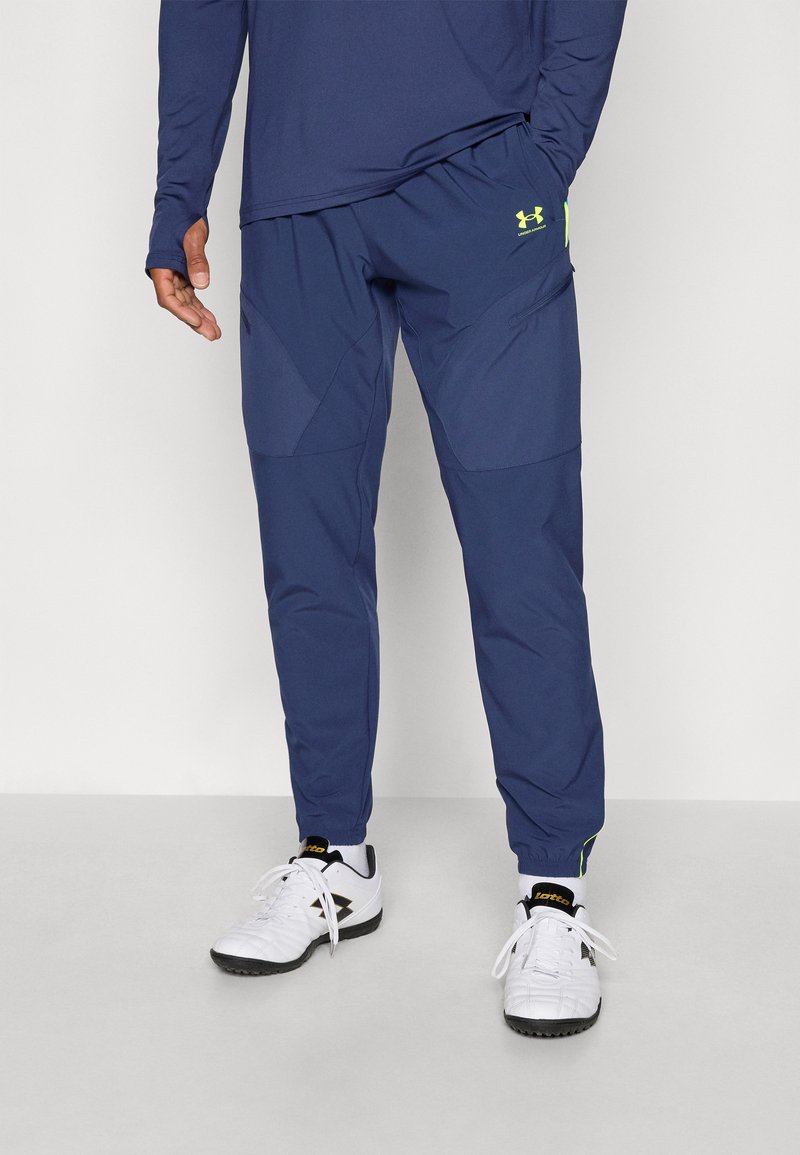 Pantalons de sport navy à coupe fuselée, avec une finition texturée, des poignets élastiques et un logo Under Armour en vert fluo.