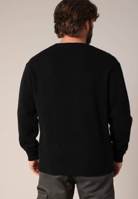 Zwarte gebreide trui met een ronde hals, lange mouwen en geribbelde zoom; heeft een zachte textuur en een losse pasvorm.