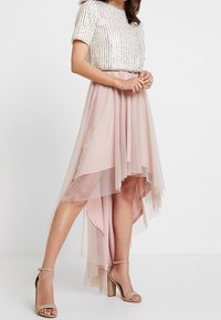 Pärlad kortärmad topp i kombination med en blushrosa hög-låg tullekjol, med ett lagerdesign och genomskinlig textur, kompletterad med beige klackar.