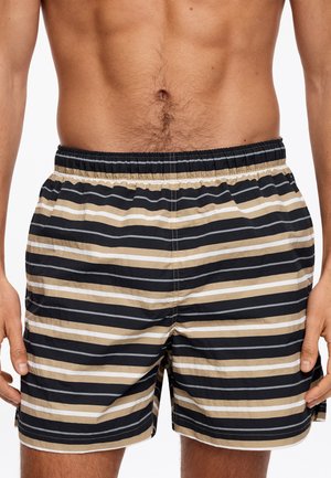Torse masculin portant un short de bain à rayures horizontales beige, noir et blanc avec une ceinture élastique, debout les mains détendues le long du corps.