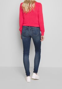 Suéter corto rosa, ajustado, de punto texturizado; combinado con jeans skinny azules, con bolsillos traseros, usados con zapatillas blancas.