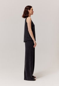 Ciemnoszara, bezrękawnik o luźnym kroju, zestawiona z pasującymi spodniami typu wide-leg. Miękka tekstura, prosta sylwetka, minimalistyczny design.