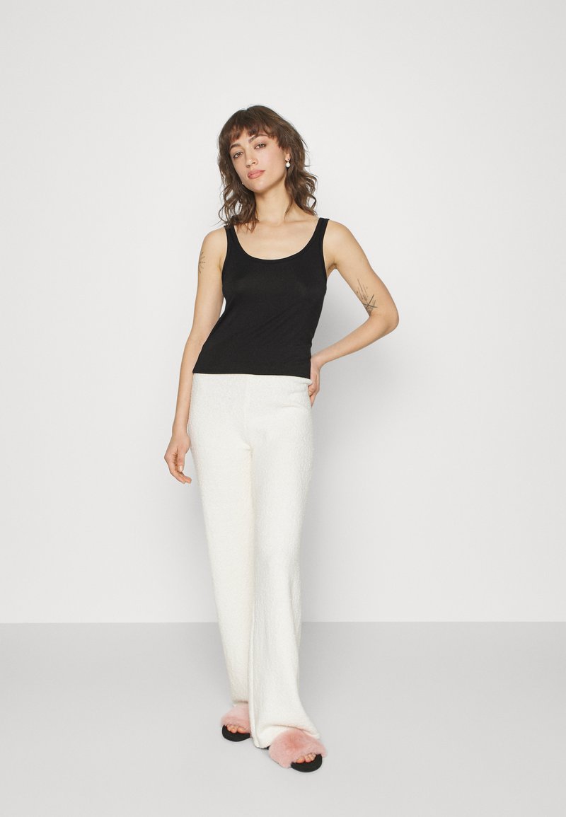 Black fitted tank top, textured white wide-leg pants, and black sandals with pink fuzzy accents. Simple, modern silhouette.