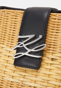 Rottinkikori, jossa musta nahkahihna ja hopeinen tunnusmerkki. Suunnitelmassa yhdistyvät luonnollinen tekstuuri ja kiillotettu metalli.