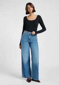 Svart langermet bodysuit kombinert med høyt liv og vide lyseblå jeans, med en klassisk denimstruktur og en sølvknapplukking.
