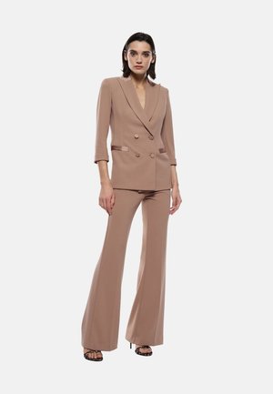 Blazer doppiopetto e pantaloni svasati in materiale beige chiaro. Il blazer presenta spalline, rever a punta e dettagli con bottoni.