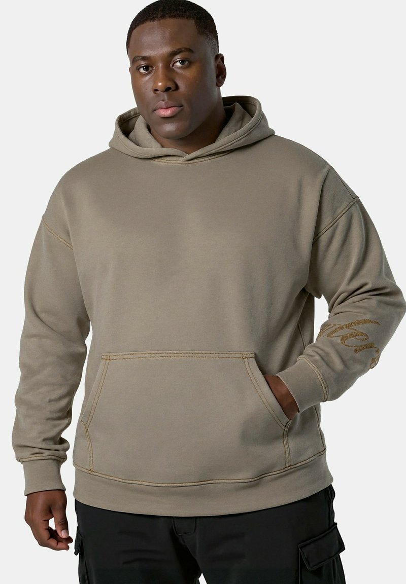 Khaki bluza z kapturem wykonana z miękkiego materiału, z przednią kieszenią i tekstowym akcentem na rękawie. Gładka tekstura i luźny krój.