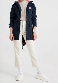 Marineblå vandtæt jakke med pink hætteforing, hvide cropped jeans og hvide sneakers med tekstureret mønster og tykke såler.