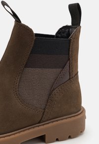 Stivaletto in suede marrone con pannelli elastici laterali in marrone scuro e nero, suola in gomma con battistrada testurizzato e linguetta sul retro.
