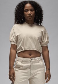 Maglietta beige cropped con maniche a palloncino e orlo elastico, abbinata a pantaloni a vita alta coordinati. Tessuto morbido e dettagli di cucitura delicati.