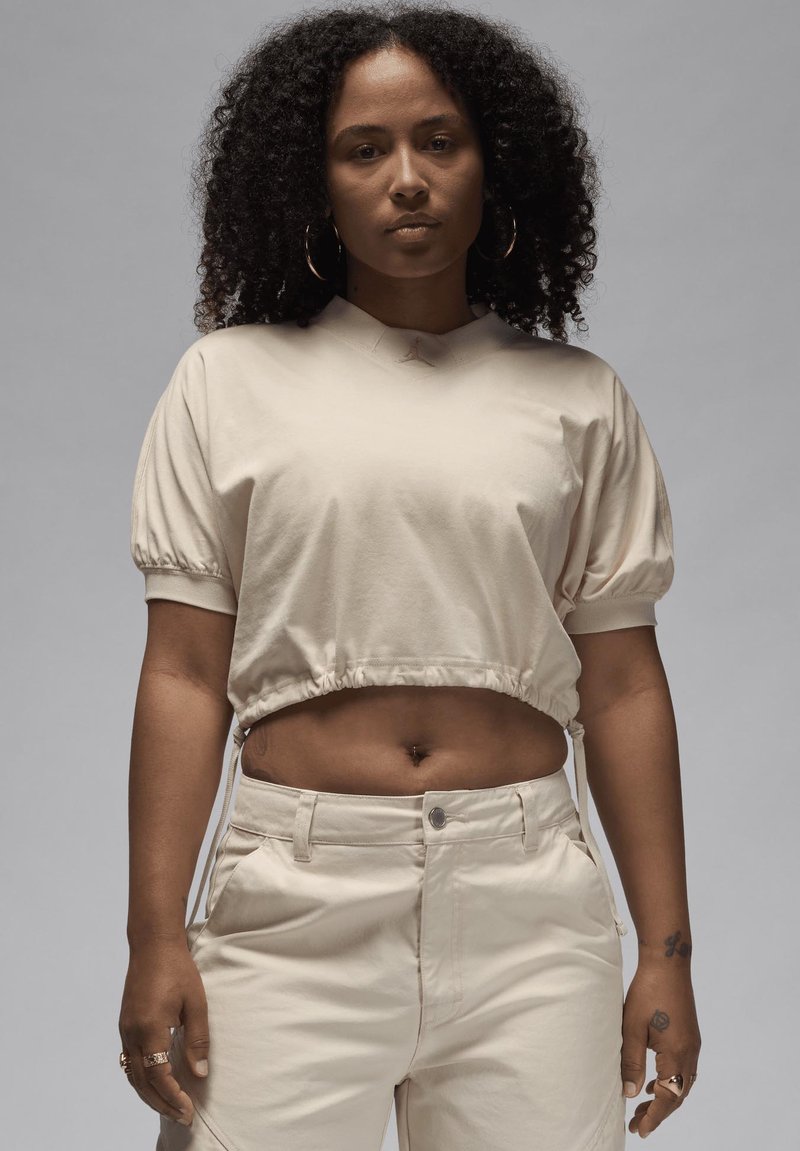 Maglietta beige cropped con maniche a palloncino e orlo elastico, abbinata a pantaloni a vita alta coordinati. Tessuto morbido e dettagli di cucitura delicati.