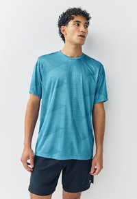 Ljusblå träningsskjorta med diamantmönster, korta ärmar, rund halsringning, kombinerad med svarta shorts. Slät textur, lättviktstyg.