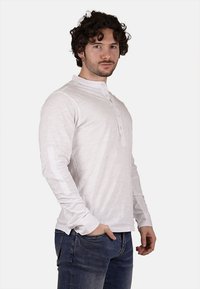 Camicia henley a maniche lunghe bianca con placket bottonato, texture a coste e pannelli delle maniche a contrasto, abbinata a jeans in denim scuro.