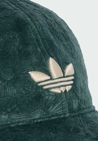 Gorra verde con un patrón floral texturizado, que presenta un logotipo bordado en color crema. Forma redondeada con un visera curva y un sutil brillo.