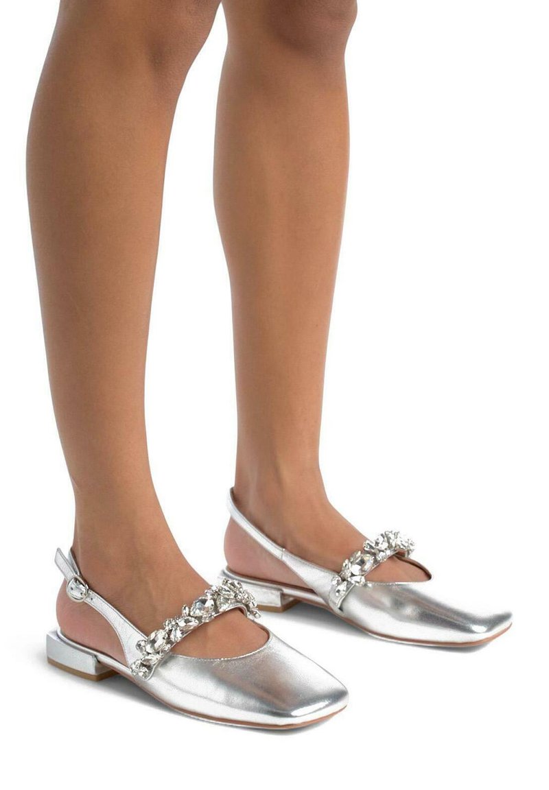 Scarpe piatte metalliche argento con punta quadrata e tacco basso, caratterizzate da una fascia decorativa di gioielli sulla parte anteriore.