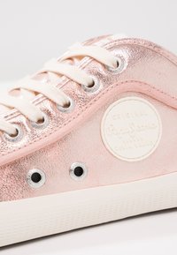 Metalické růžové tenisky s texturovaným svrškem, smetanovými tkaničkami, kulatou bílou nášivkou, stříbrnými očky a bílou gumovou podrážkou.