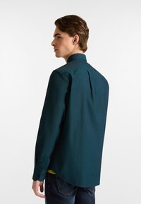 Donkerblauwe blouse met lange mouwen, een button-down kraag, een rugplooi en een afgeronde zoom. De stof lijkt glad met een lichte glans.