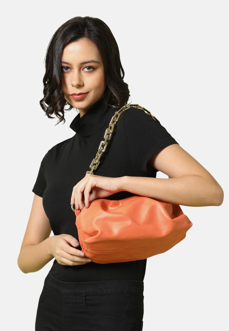 Borsa a tracolla in ecopelle arancione con un design morbido e soffice, dotata di una tracolla in catena dorata. La texture liscia e i dettagli cuciti sono ben visibili.