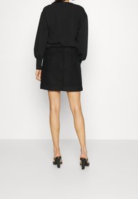 Zwarte trui met ballonmouwen gecombineerd met een getextureerde zwarte minirok. Aan de voeten zwarte sandalen met hoge hak en een stevige hak.